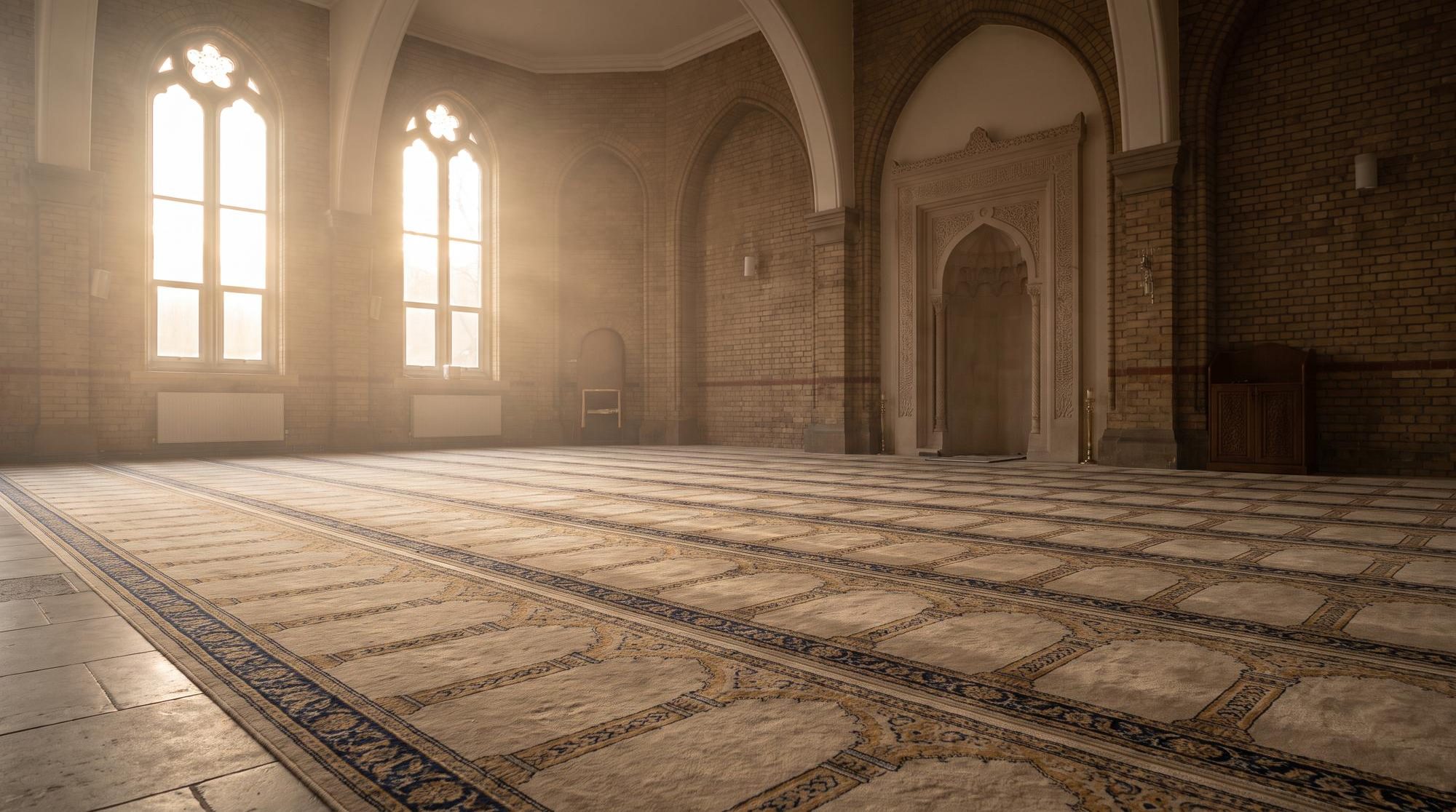 An empty mosque prayer hall at dawn with rows of patterned carpet and light through arched windows