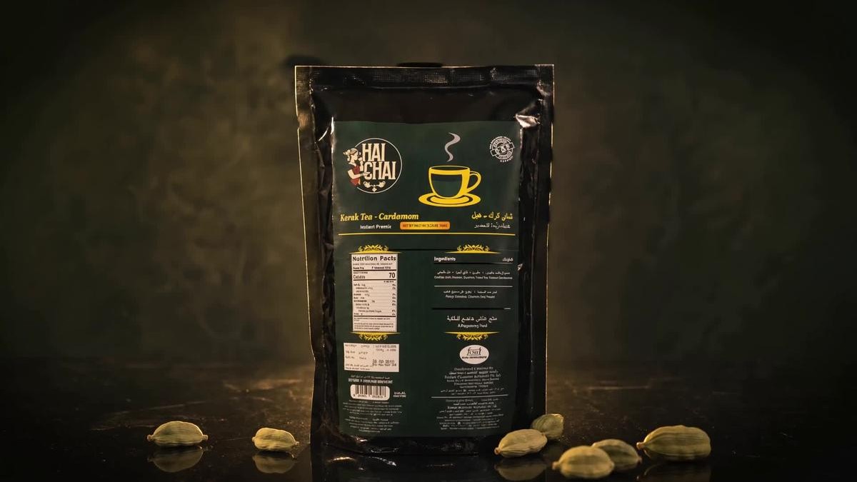 A Hai Chai Karak Tea Cardamom pouch standing on a dark surface, with cardamom pods in front